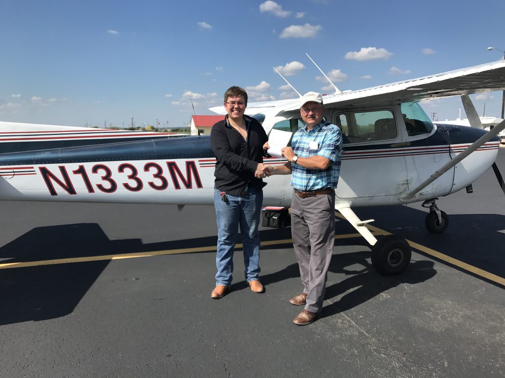 Two men (student and instructor) standing in front of a blue and white Cessna 172L arplane. The student has just earned his pilot license