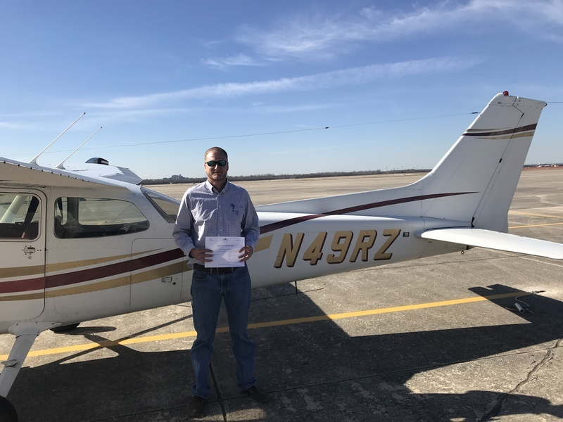 Man standing in front of a white Cessna 172 holding a paper pilot certificate